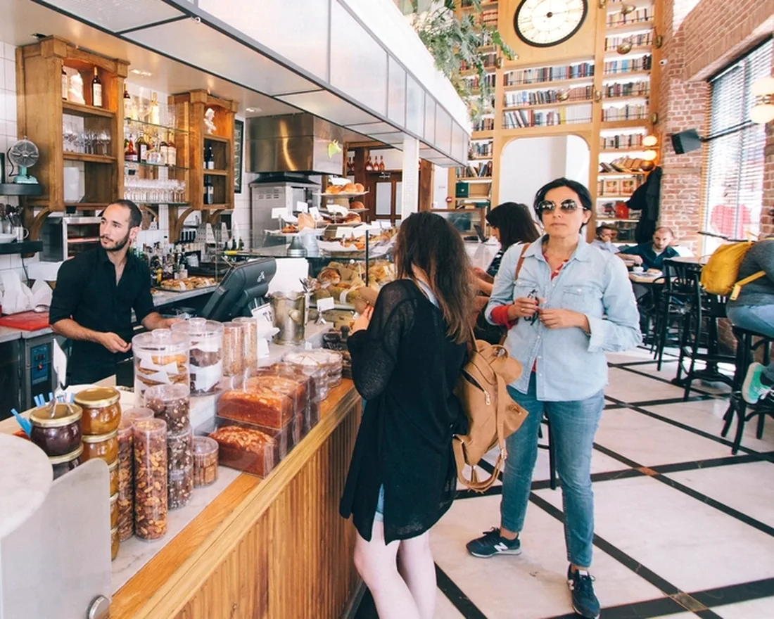 Deux clientes commandent au comptoir d’un café de quartier, le barista les accueille.